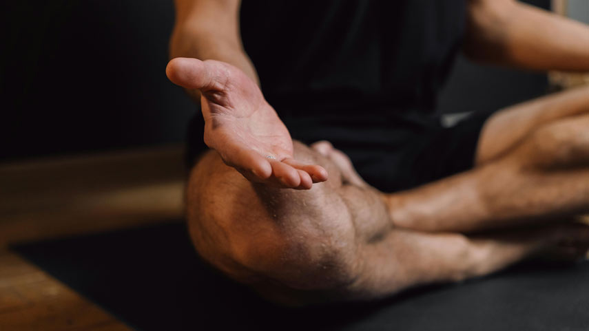 Homme assis les jambes croisées sur un tapis de yoga, les bras tendus vers l'avant, les paumes tournées vers le haut.