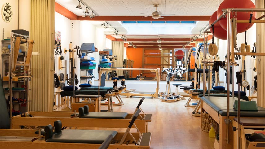Un studio d'exercice spacieux avec des appareils de Pilates, un sol en bois, des miroirs et divers accessoires de fitness bien rangés.