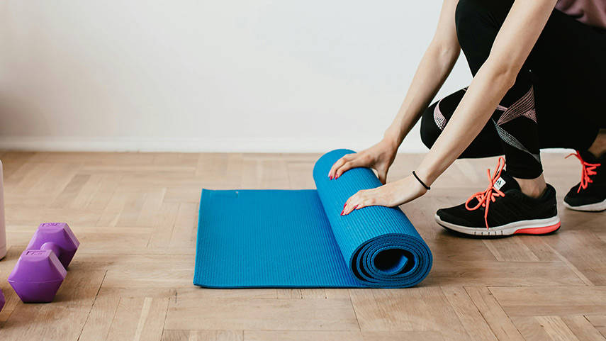 Woman placing a mat on the floor, getting ready to practice Pilates