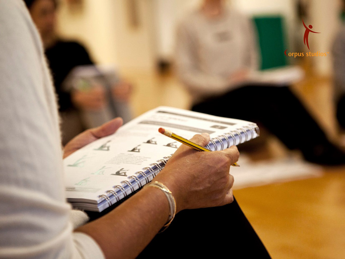 Person holding a notebook and pencil, with pages open showing text and diagrams, in a sitting position indoors.